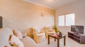 Un salon comprenant un canapé, deux fauteuils, une table basse, un téléviseur et une fenêtre.