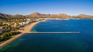 Vue aérienne d’une ville côtière avec une plage, des eaux d’un bleu limpide et des montagnes en arrière-plan.