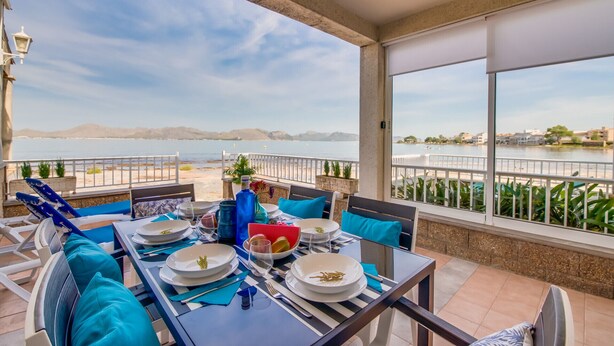 Un coin repas avec vue sur la mer, où une table est dressée avec des assiettes, des verres et une bouteille.