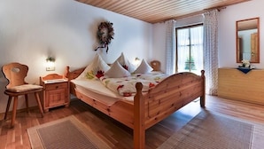 Una cama de madera con una colcha estampada, una mesita de noche con una lámpara, una silla y un espejo en la pared.