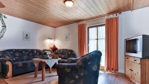 Una sala de estar acogedora con sofá, sillón, aparador de madera y televisor.