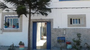 A building with a blue door, a window with a blue frame, and a small window on the side. There are potted plants outside. - Dar Rosa Bleu (Oualidia)
