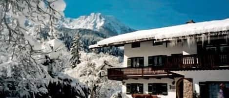 A chalet with a balcony, surrounded by snow-covered trees and mountains.