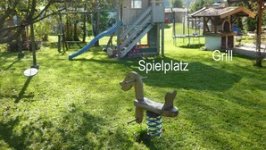 En legeplads med rutchebane og gynger, en trækonstruktion med teksten "Spielplatz" og et område til "Grill".