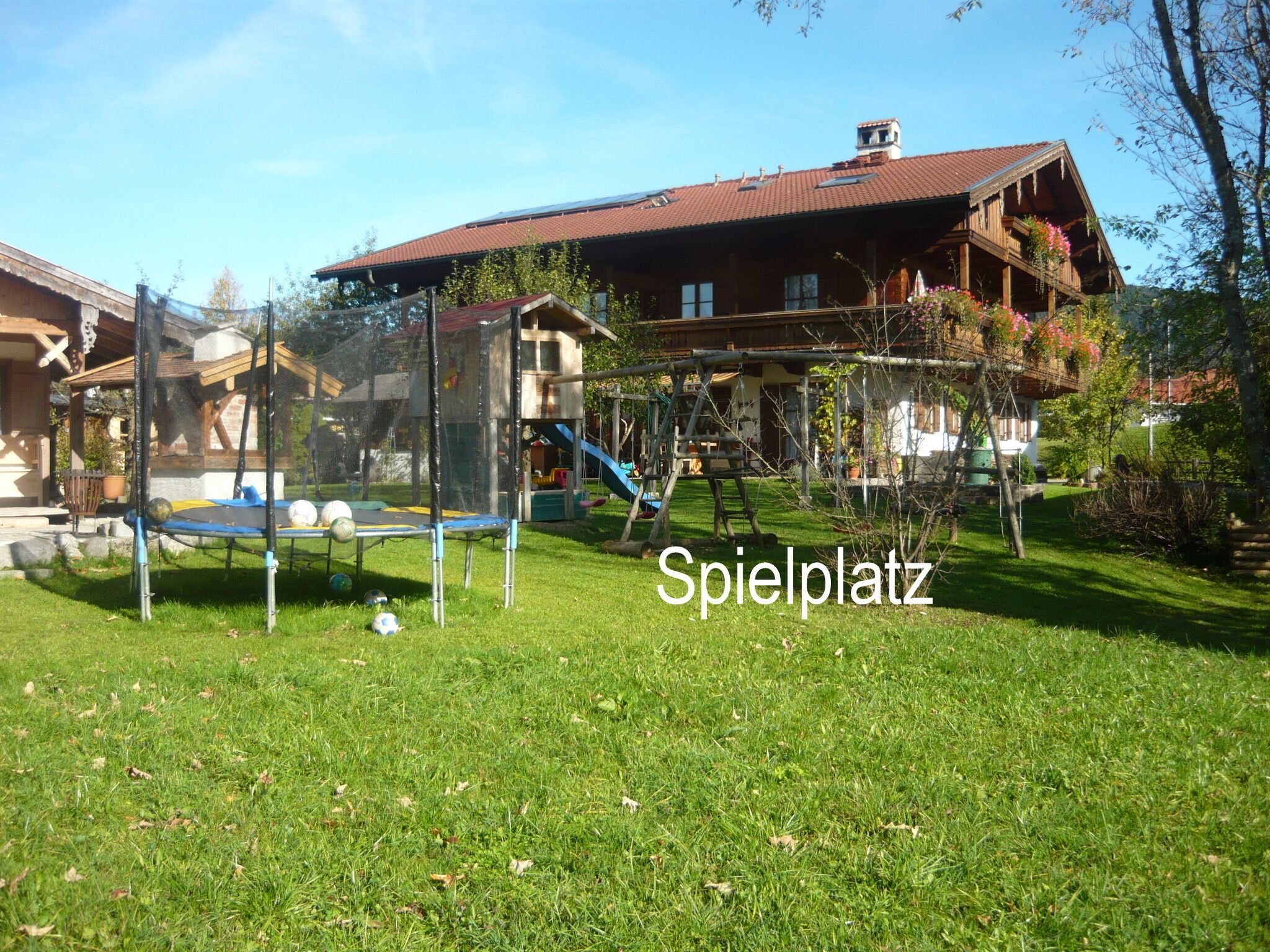 A playground with a trampoline and slides, surrounded by a well-maintained lawn and a wooden house with a red roof.