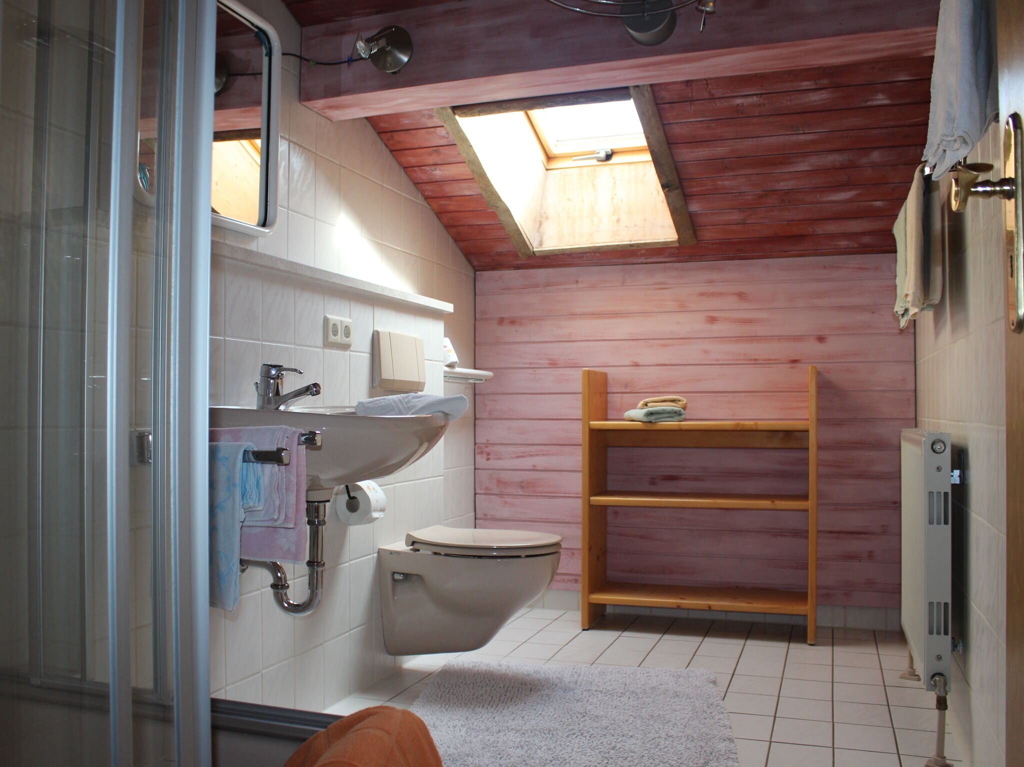 Une petite salle de bain compacte, dotée d’un puits de lumière, d’un lavabo, de toilettes et d’une étagère en bois.