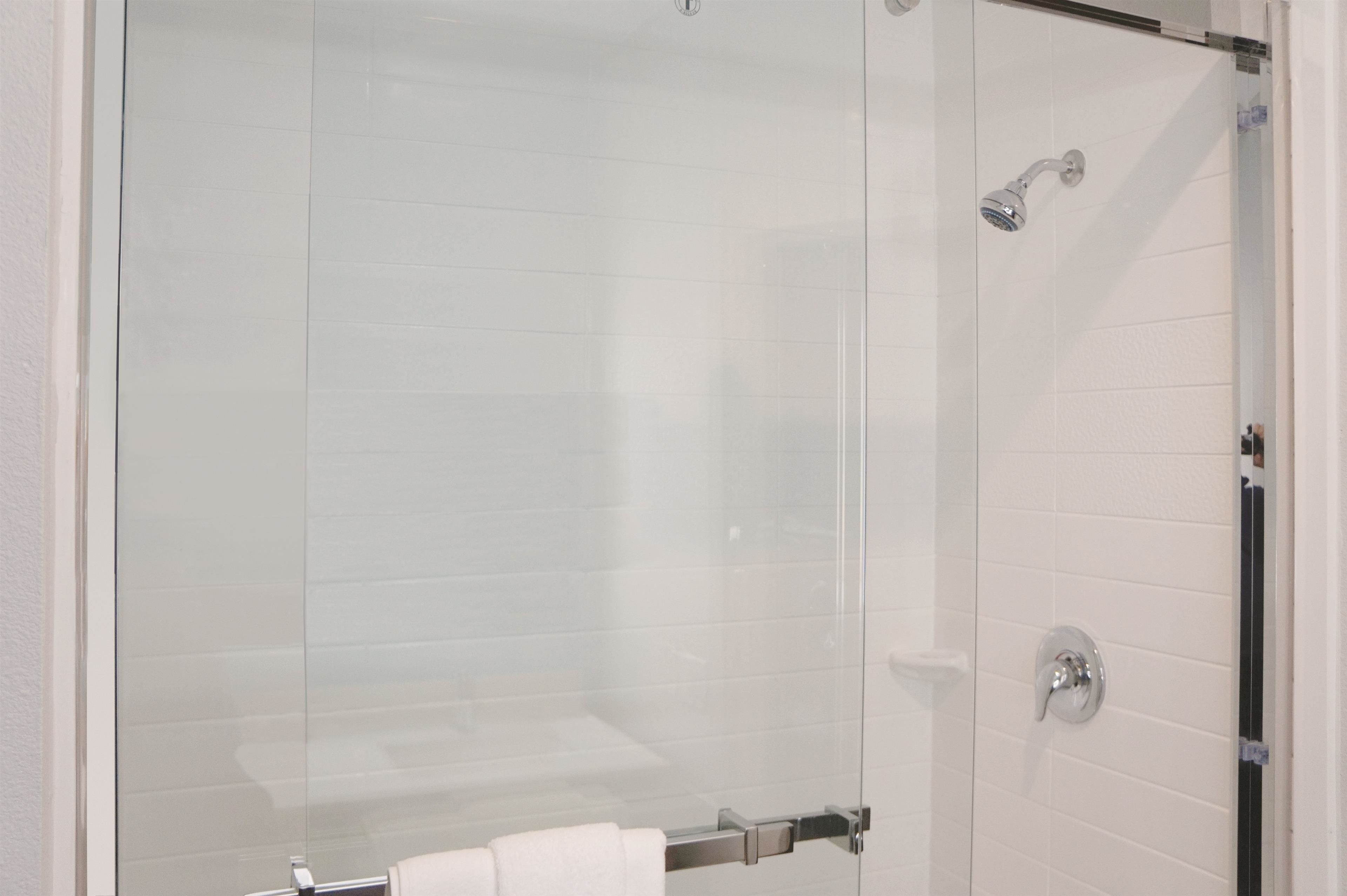 A glass-enclosed shower stall with a white tiled wall, a visible showerhead, and a towel rack.