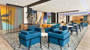 A modern lounge area with blue sofas, a patterned carpet, and a mural of a bird on the wall. - La Quinta Inn & Suites by Wyndham Richmond-Sugarland (Richmond)