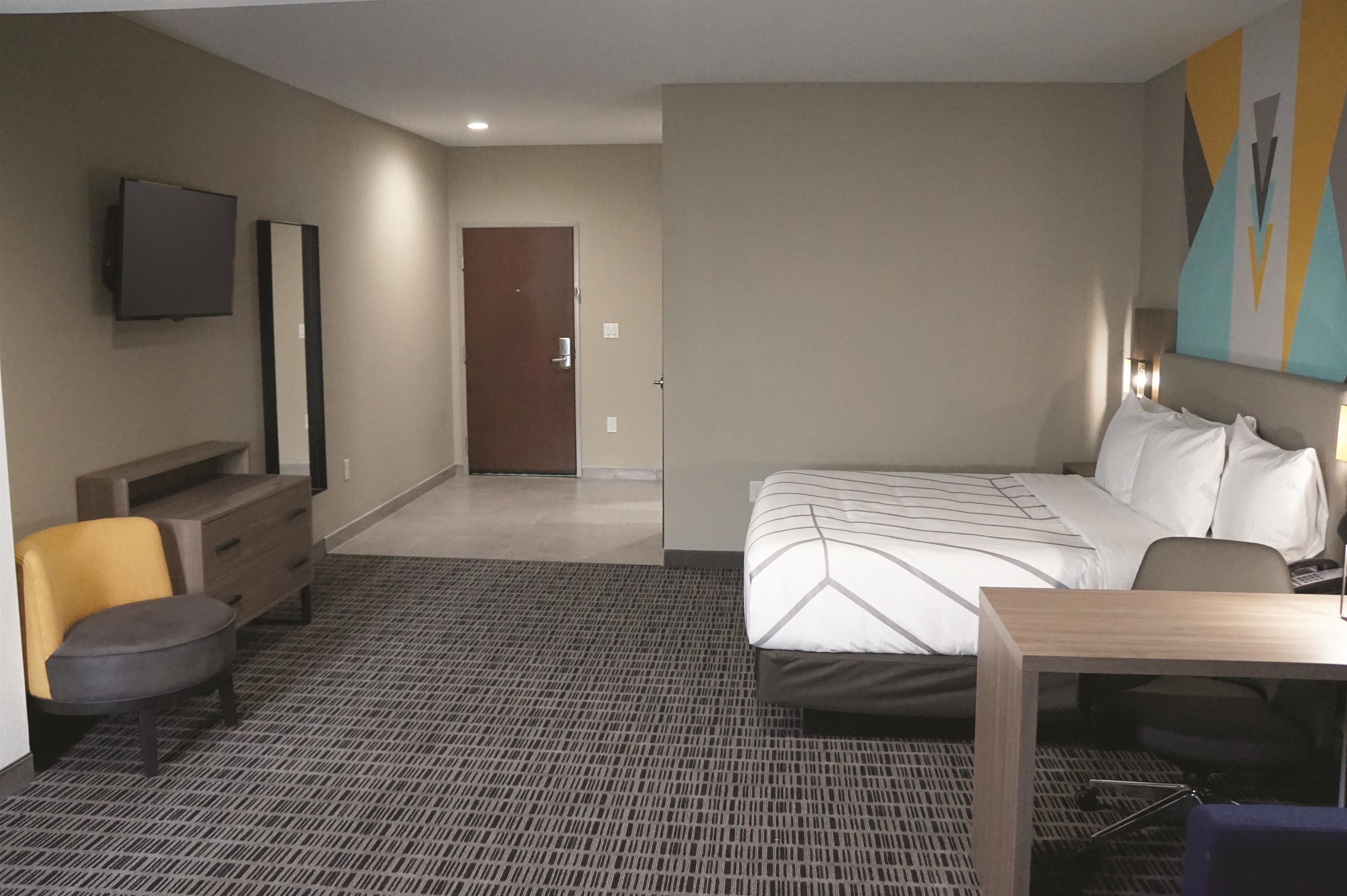 A hotel room with a bed, a desk, a chair, a TV, and a door.