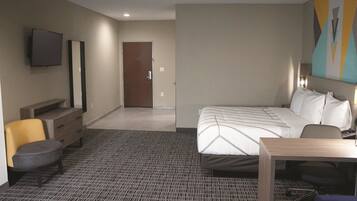 A hotel room with a bed, a desk, a chair, a TV, and a door.