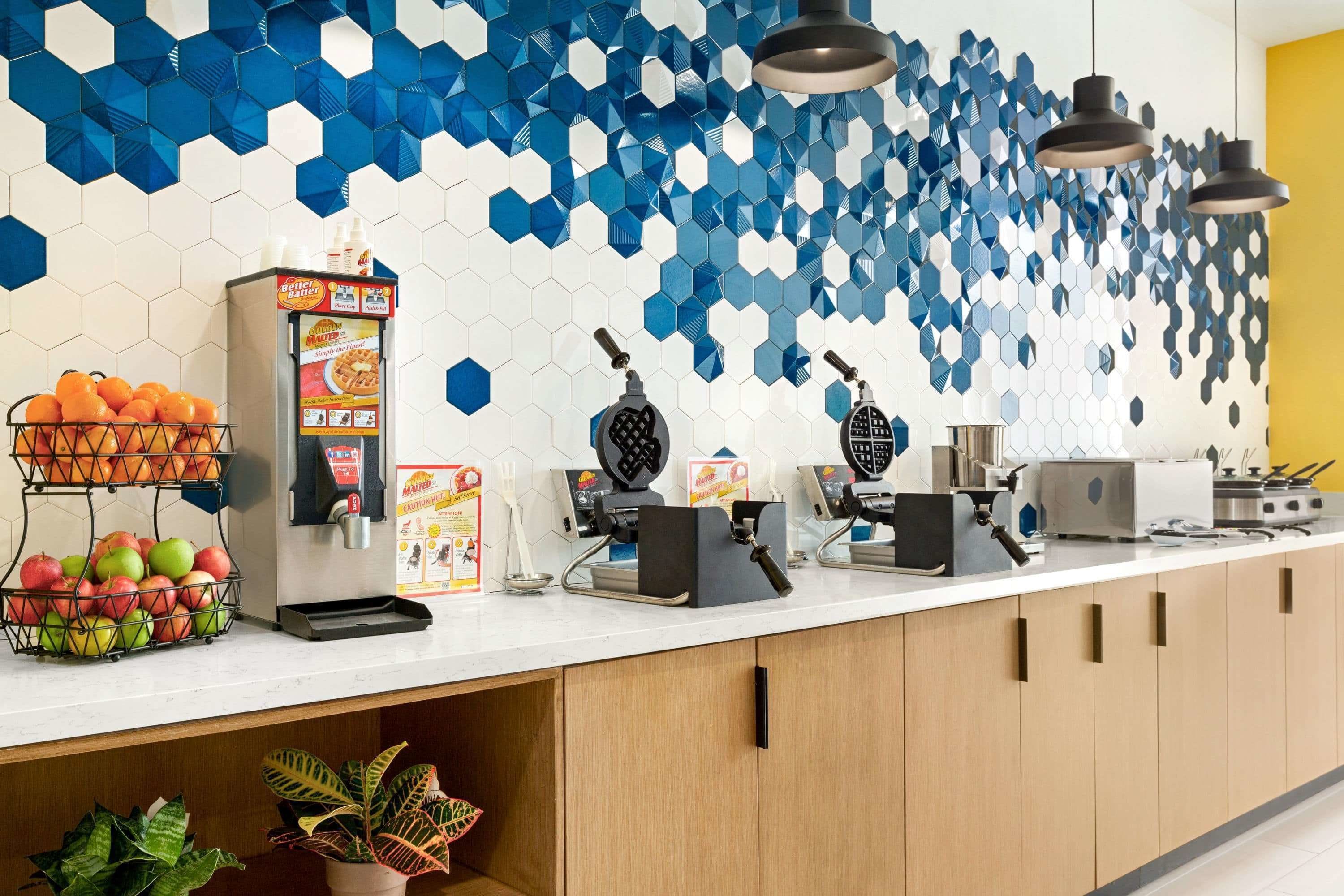 A kitchen counter with waffle makers, a fruit basket, and a coffee machine.