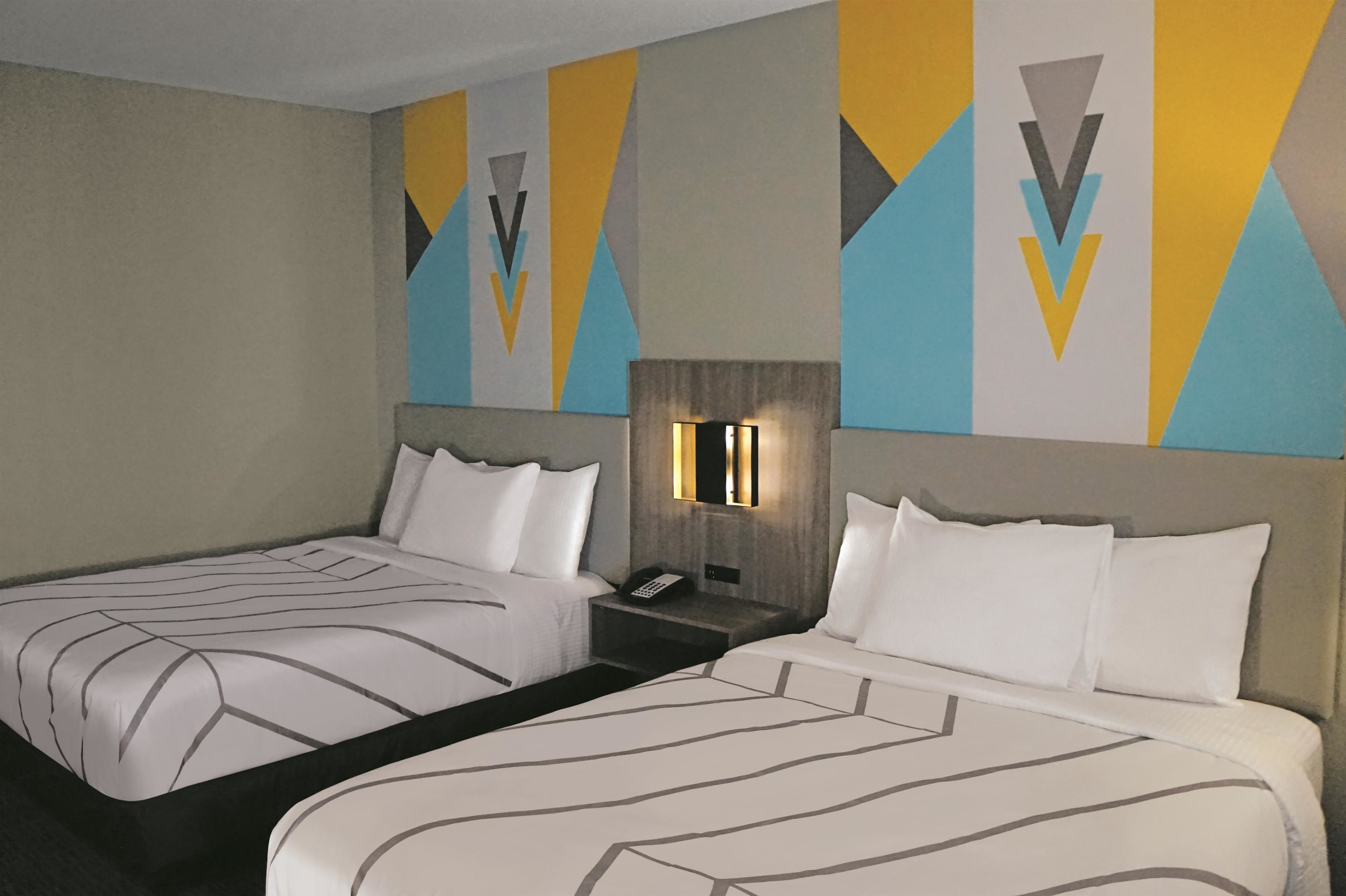 A hotel room with two beds, a nightstand with a phone, and a wall with geometric patterns.