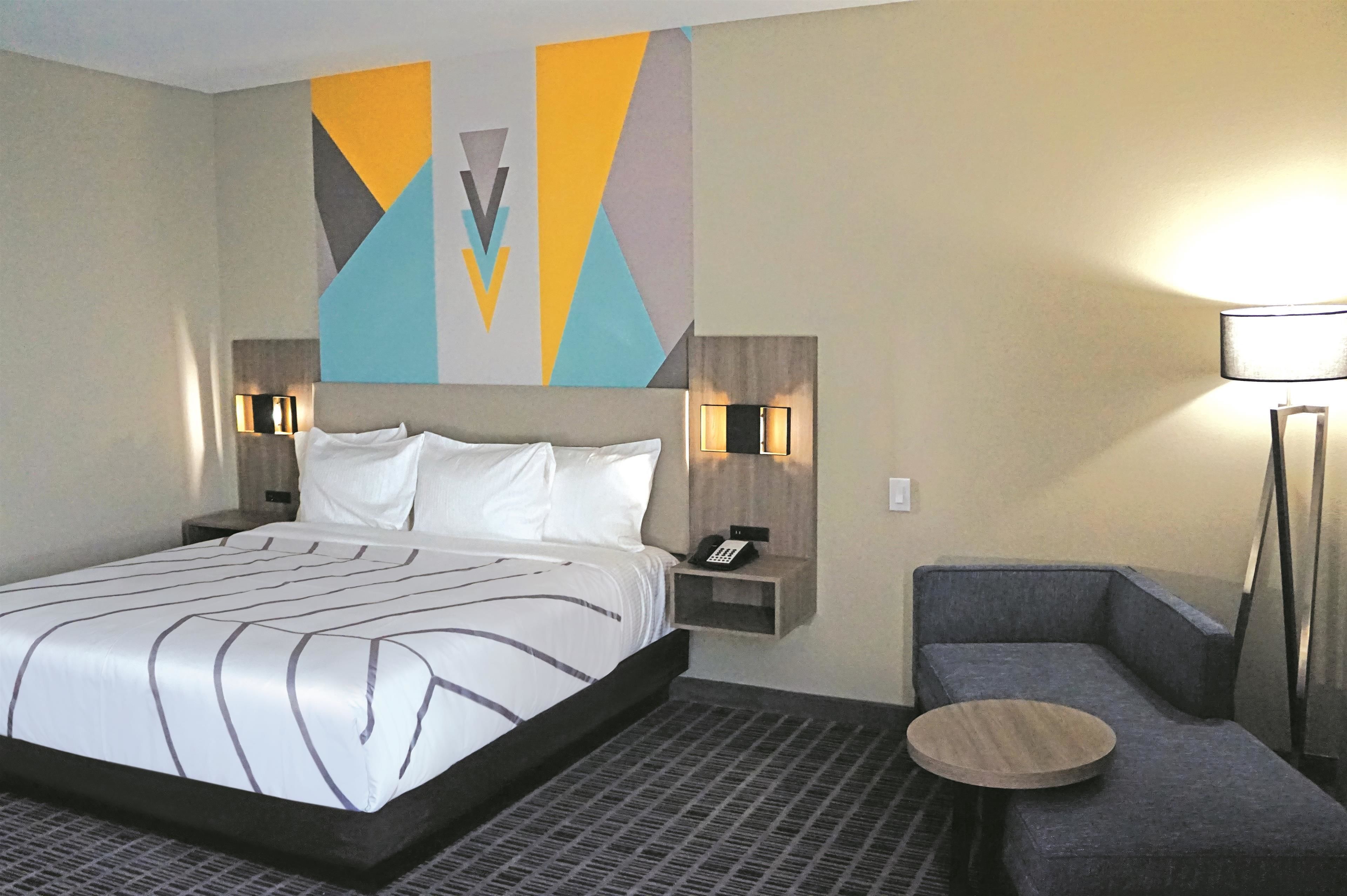 A hotel room with a large bed, bedside tables with lamps, a sofa, and a small round table.
