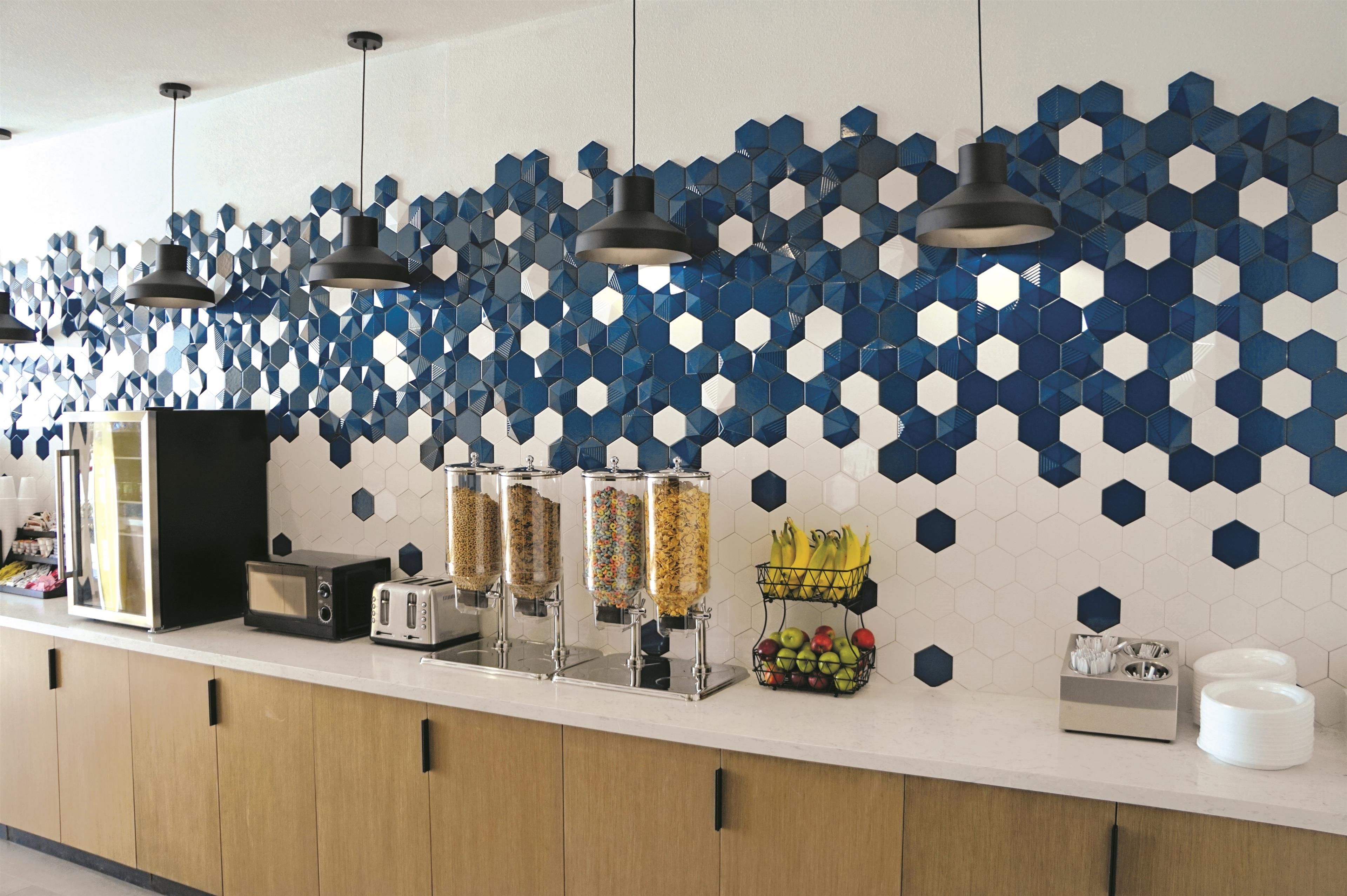 A breakfast bar with a hexagonal tile backsplash, a toaster, a refrigerator, and a fruit basket.