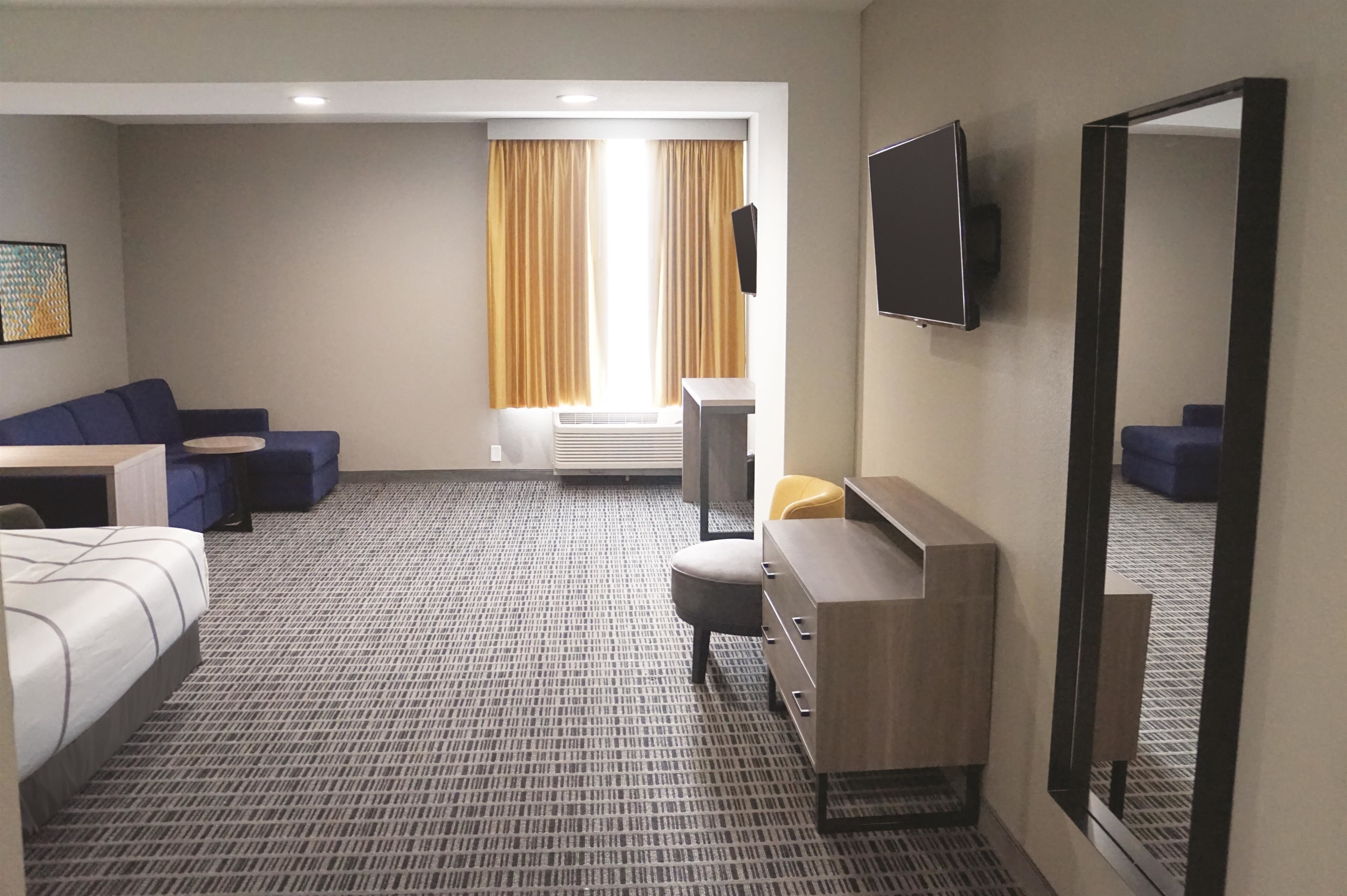 A hotel room with a bed, a desk, a chair, a TV, a mirror, and a window with curtains.