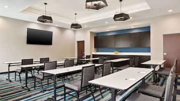 A conference room with tables and chairs, a large flat-screen TV, and pendant lighting.