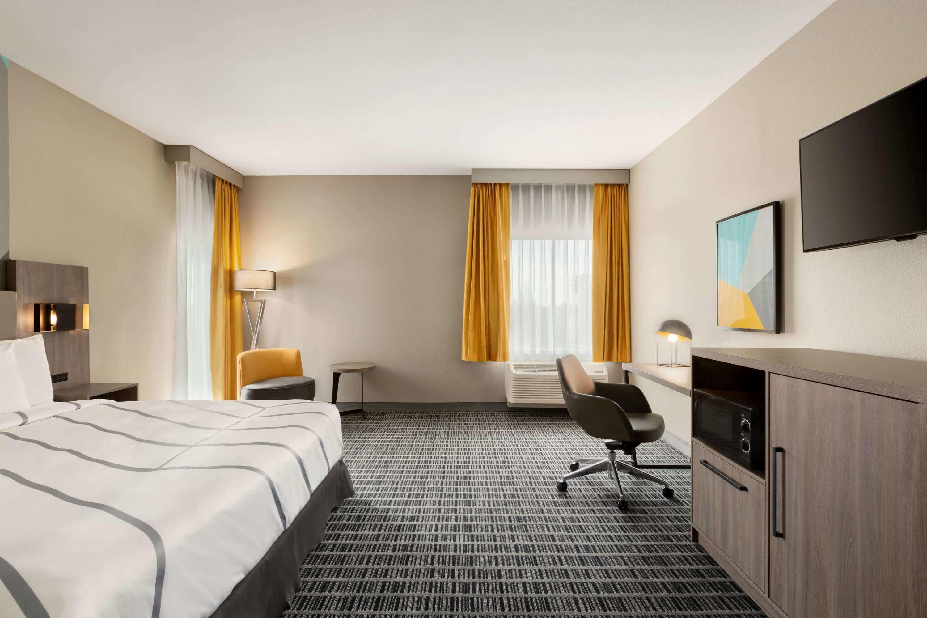 A hotel room with a bed, a desk, a chair, a TV, and a window with curtains.