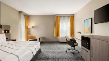 A hotel room with a bed, a desk, a chair, a TV, and a window with curtains.