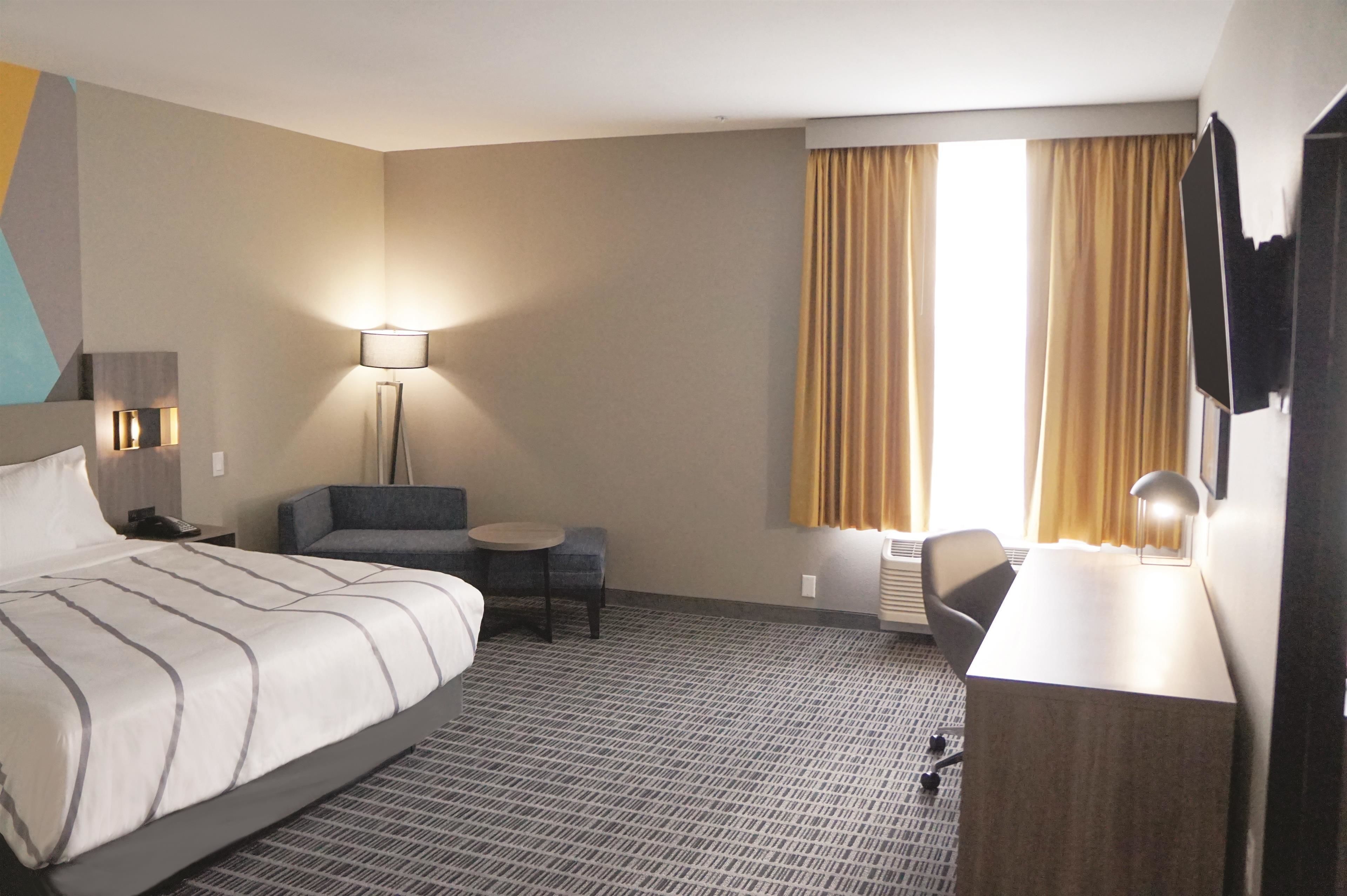 A hotel room with a bed, a desk, a chair, a lamp, and a TV.