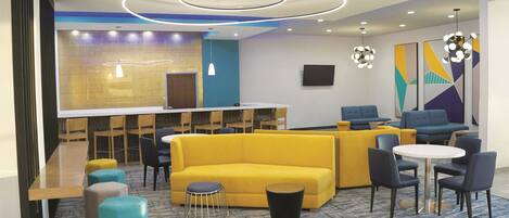 A modern lobby with a yellow sofa, blue and yellow chairs, a round table, and a patterned carpet.