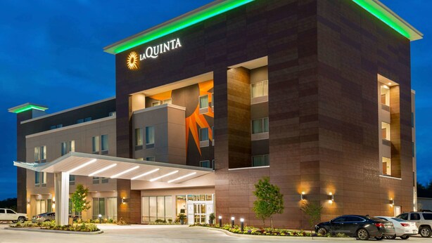 A modern hotel with a prominent logo, a covered entrance, and a well-lit facade. - La Quinta Inn & Suites by Wyndham Richmond-Sugarland (Richmond)