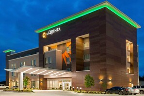 A modern hotel with a prominent logo, a covered entrance, and a well-lit facade.