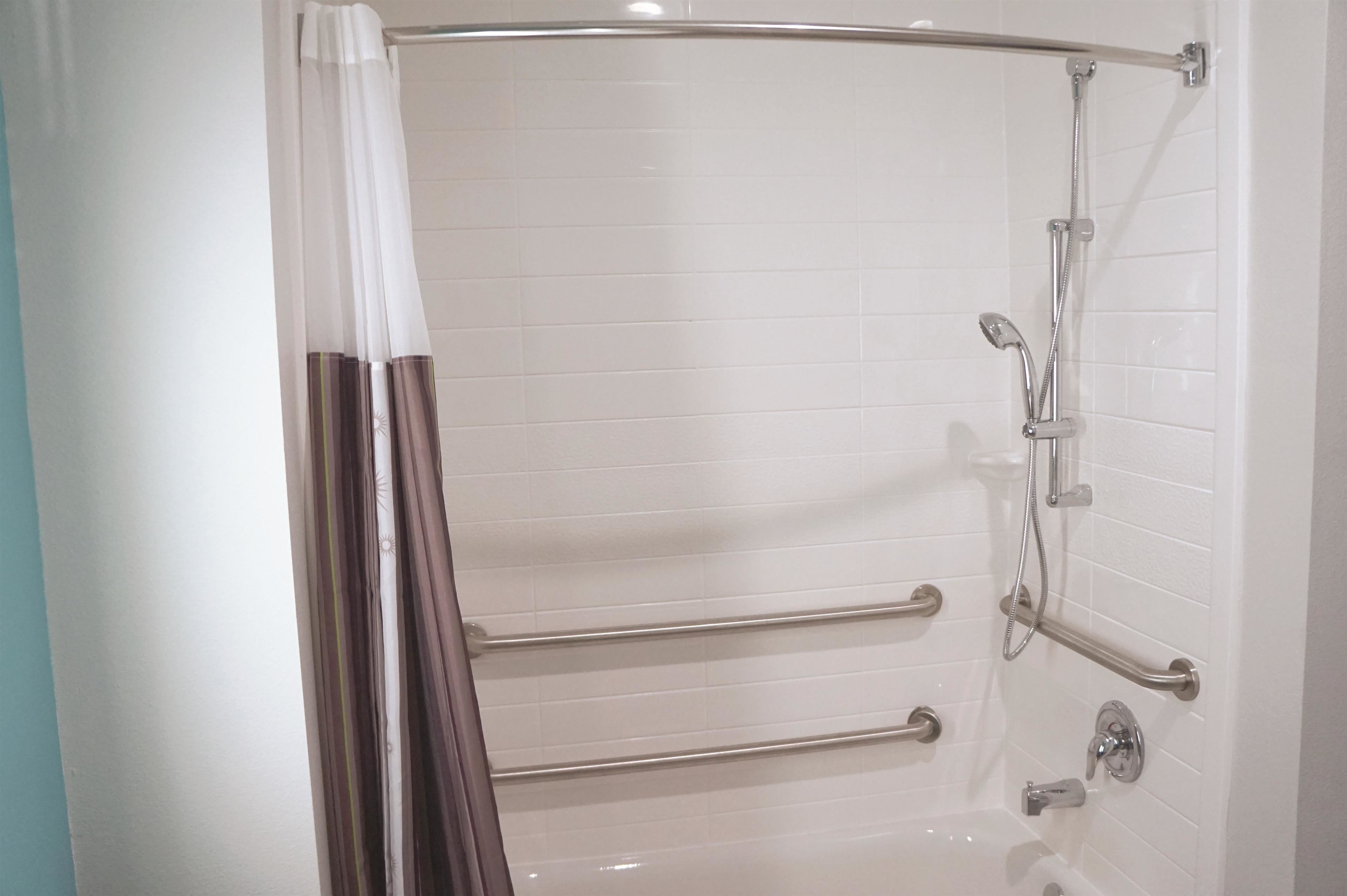 Un baño moderno con paredes de azulejos blancos, una ducha con puerta de cristal y barras de apoyo.