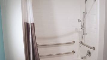 Un baño moderno con paredes de azulejos blancos, una ducha con puerta de cristal y barras de apoyo.