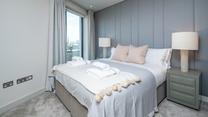 Une chambre d’hôtel moderne avec un grand lit, deux lampes de chevet, une vue sur la ville et un panneau de commande au mur.