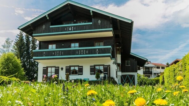 A two-story chalet with a sloped roof, wooden exterior, and a balcony on the upper floor. - Vacation apartment 7 for up to 4 people, with 2 extra bedrooms and kitchen in the living/dining area (Reit im Winkl)