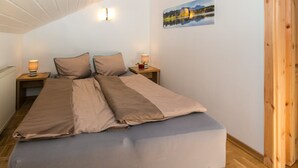 A bedroom with a bed, two bedside tables, a nightstand, a radiator, a wooden floor, and a painting on the wall. - Vacation apartment 7 for up to 4 people, with 2 extra bedrooms and kitchen in the living/dining area (Reit im Winkl)