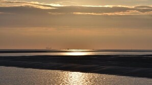 A sunset over a calm sea with a distant ship. - Directly at the Wadden Sea, part of UNESCO World Heritage. Calm/Fun at beach (Wierum)