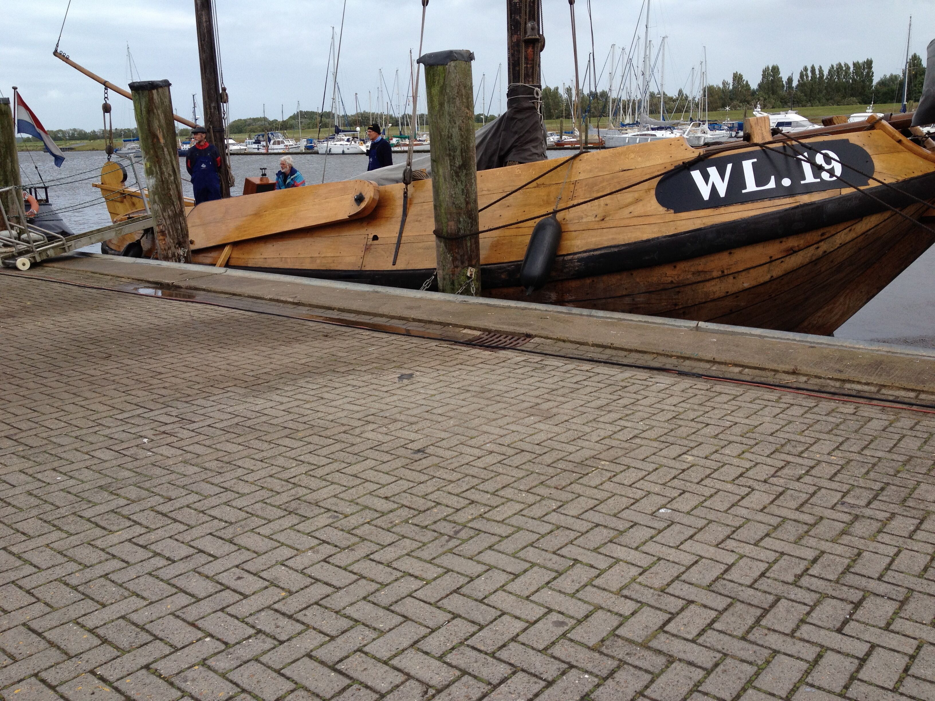 Un bote de madera amarrado en un puerto deportivo, con un número de registro visible.