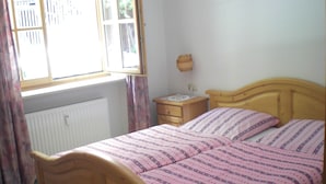 A bedroom with a wooden bed, a nightstand, a window with curtains, and a radiator.