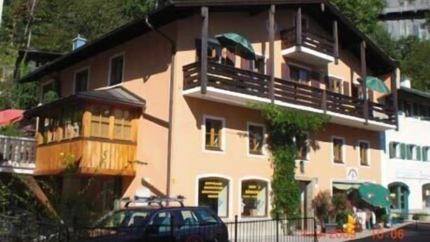 A two-story building with balconies, a wooden fence, and a car parked in front.