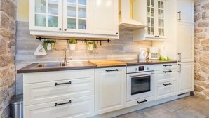A modern kitchen with white cabinetry, a built-in oven, and a stone wall backdrop. - Rustic holiday house KATE (Čižići)