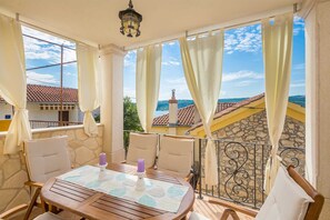 A balcony with a table, chairs, and a view of the sea and buildings. - Rustic holiday house KATE (Čižići)