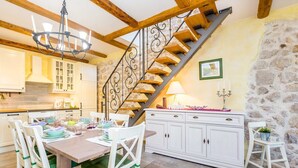 A dining area with a wooden table and chairs, a staircase with a wrought iron railing, and a stone wall. - Rustic holiday house KATE (Čižići)