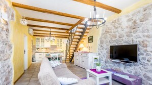 A cozy living room with a sofa, a TV, and a staircase leading to a kitchen. - Rustic holiday house KATE (Čižići)