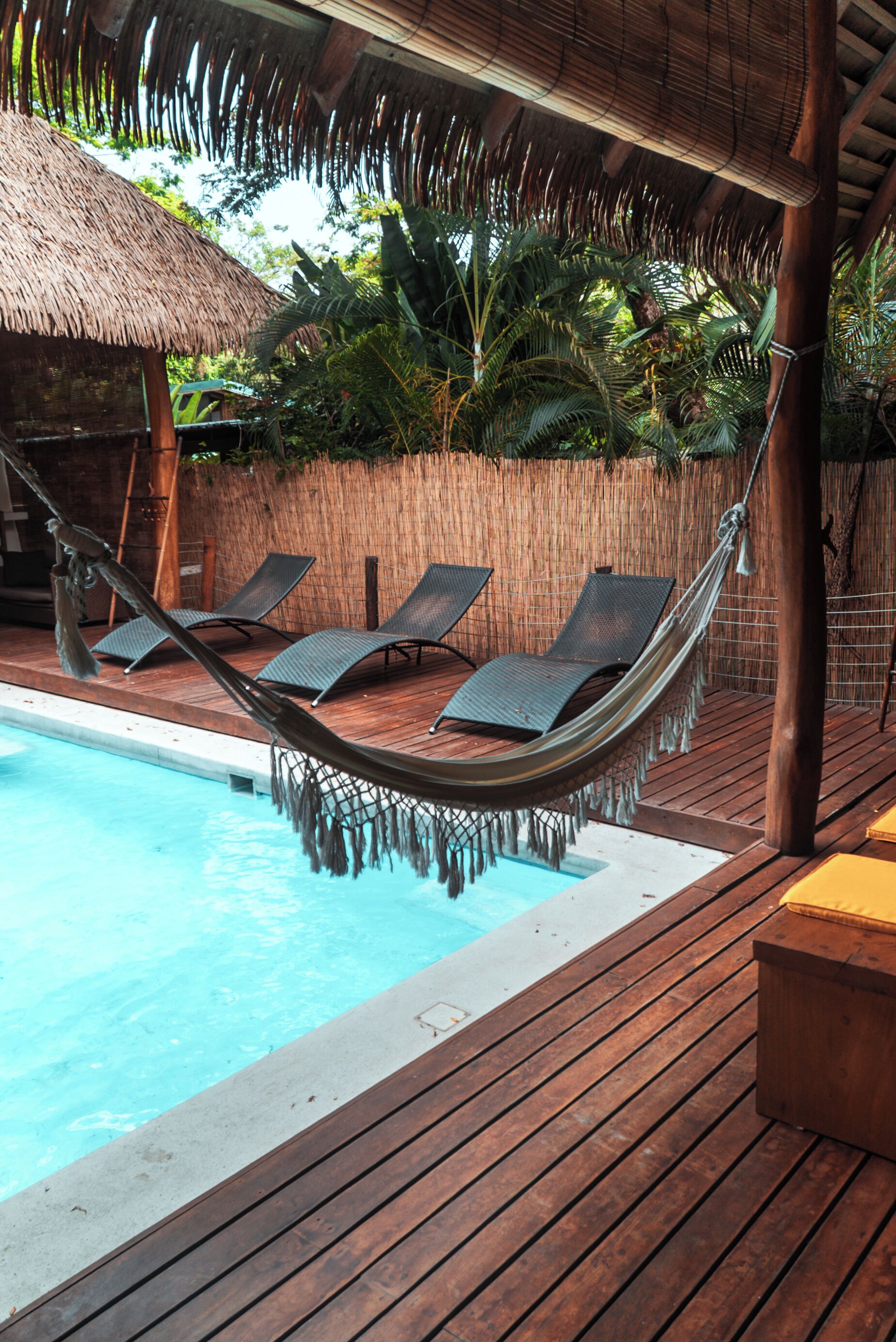 A poolside area with a hammock, lounge chairs, and a wooden deck.