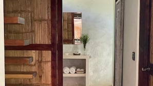 Un pasillo con una escalera de madera que lleva a una habitación. Se observa una estantería con toallas enrolladas y una planta pequeña.