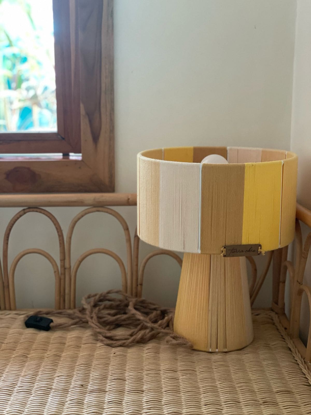 A lamp with a wooden base and a striped lampshade on a woven chair.