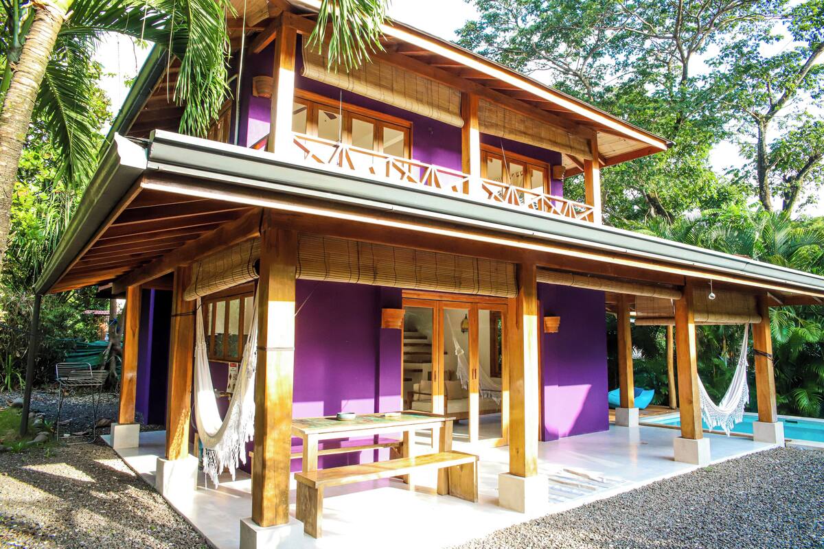 A two-story building with a wooden exterior, a balcony with white railings, and a pool area.