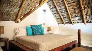 Un dormitorio con cama de madera, techo de paja y una pequeña lámpara fijada a la pared.