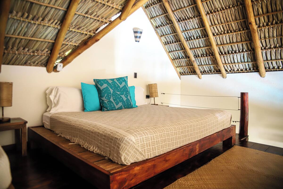 A bedroom with a wooden bed, a thatched roof, and a small wall-mounted light fixture.