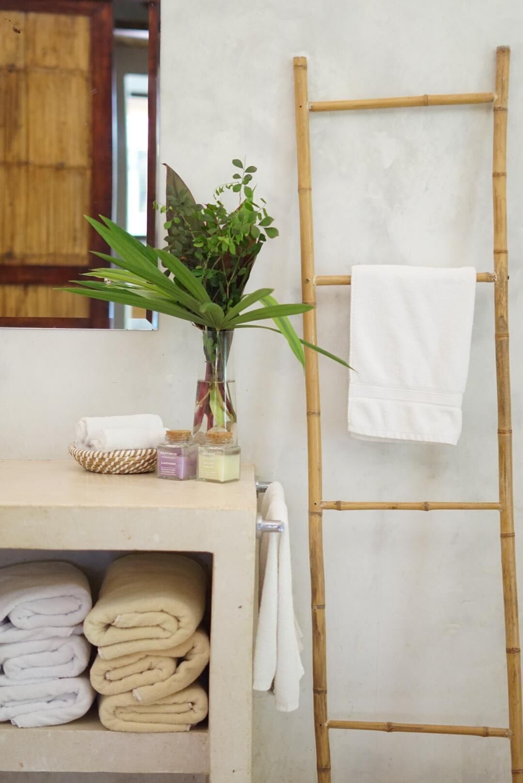 A bathroom with a bamboo ladder, a shelf with folded towels, a potted plant, and a white towel hanging on the wall.