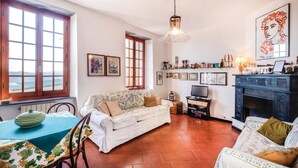 A cozy living room with a sofa, a dining table with a green tablecloth, a fireplace, and a large window overlooking a scenic view. - 2 bedroom amazing home in Carro (SP) (Carro (SP))