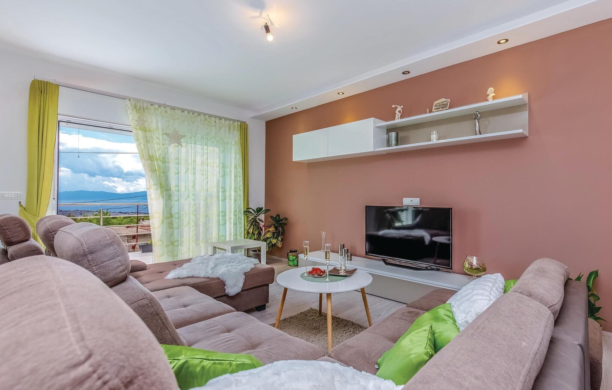 A modern living room with a sofa set, a TV, a small table with drinks, and a view of the outdoors.