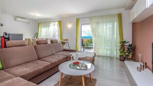 A modern living room with a brown sofa, a round coffee table with drinks, and a balcony with yellow curtains. - Stunning home in Smrika with sauna (Smrika)