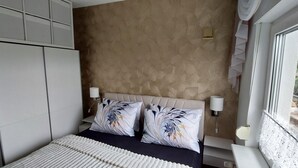 Ett sovrum med en säng, två dekorativa kuddar, en sänggavel, sänglampor och ett fönster med utsikt över grönområden utanför.